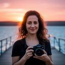 Portrait of Hatice Sulo holding a camera near a lakeside boardwalk at sunset