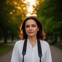 Portrait of Etleva Thamer standing with a camera strap in a quiet urban park during golden hour
